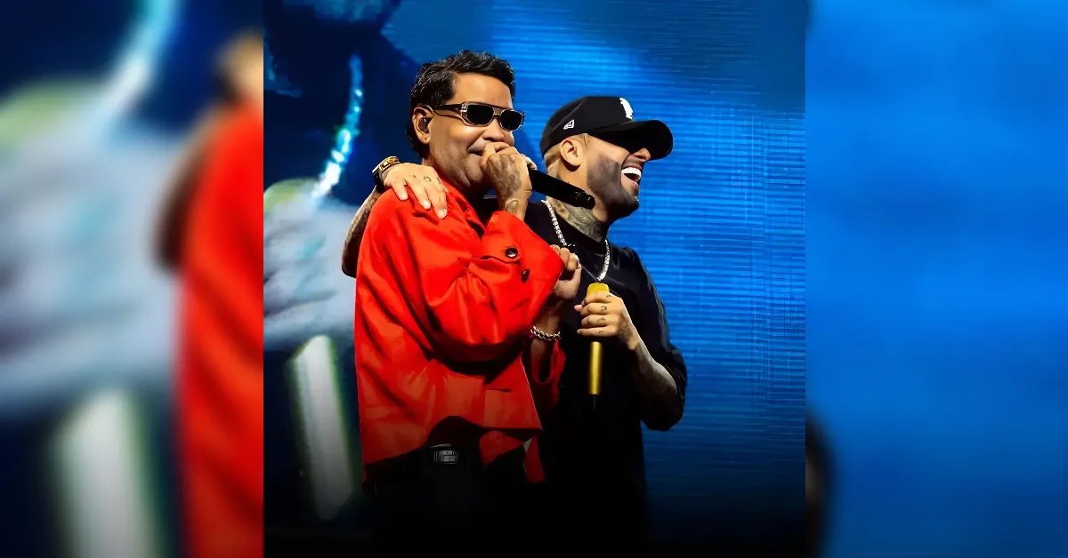 Two male performers on stage singing into microphones, one in a red jacket and sunglasses, the other in a black cap smiling beside him.