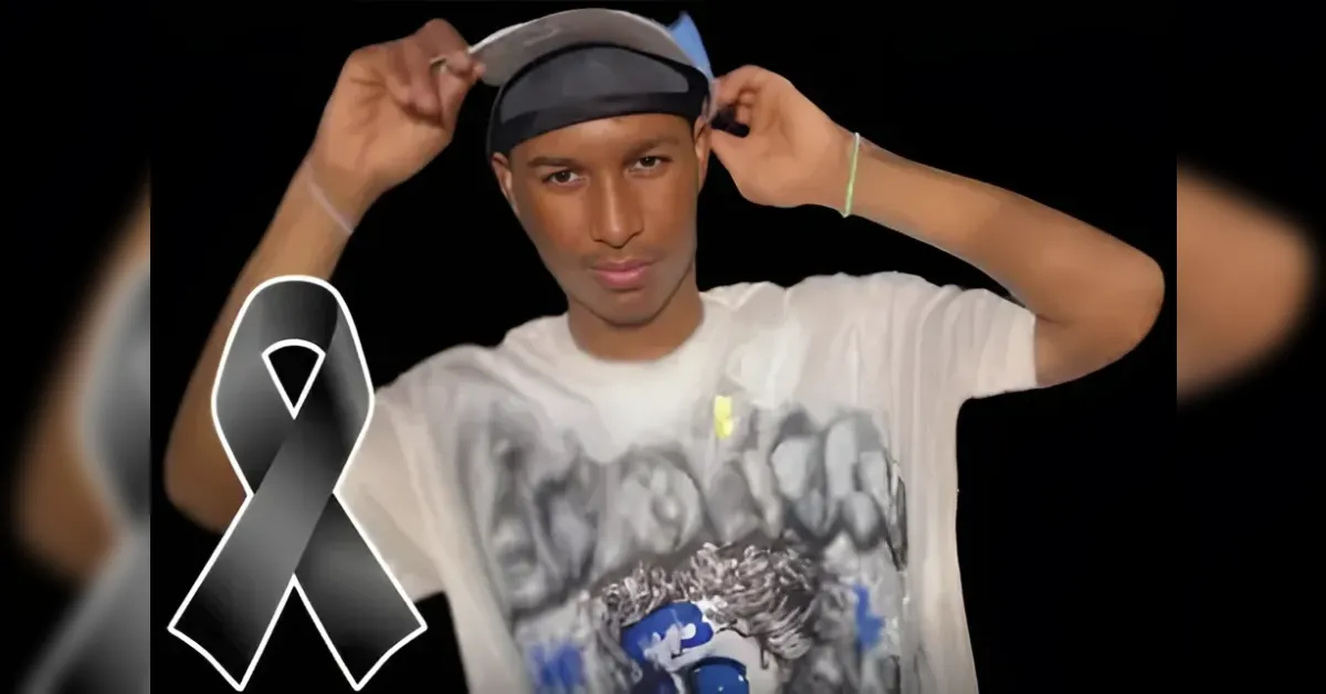Young man in a white graphic T-shirt adjusts his cap against a black backdrop with a large black awareness ribbon overlay on the left side.