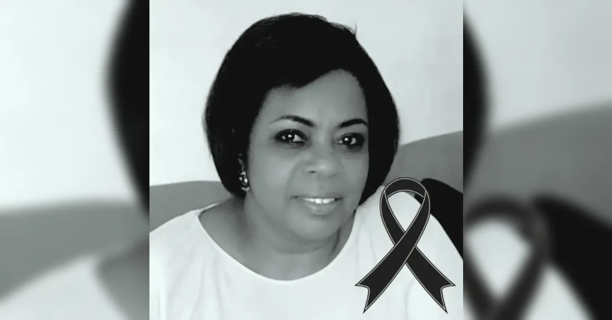 Black-and-white portrait of a smiling woman with a breast cancer awareness ribbon on her shoulder.