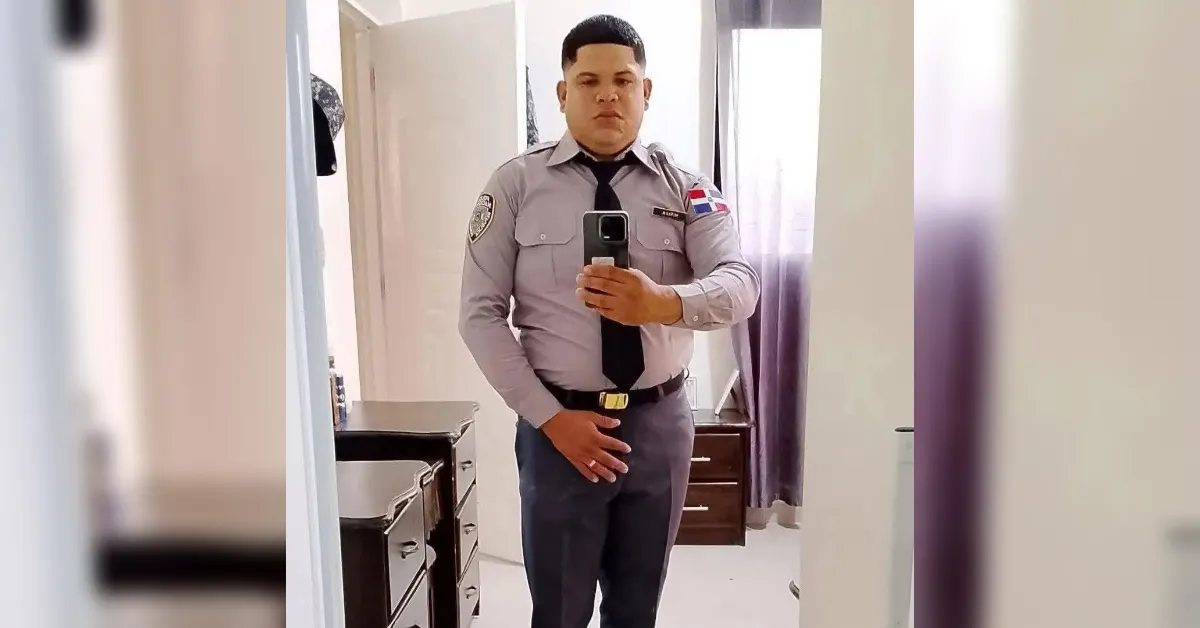 Male police officer in a gray uniform posing for a mirror selfie in a bedroom or dressing area.
