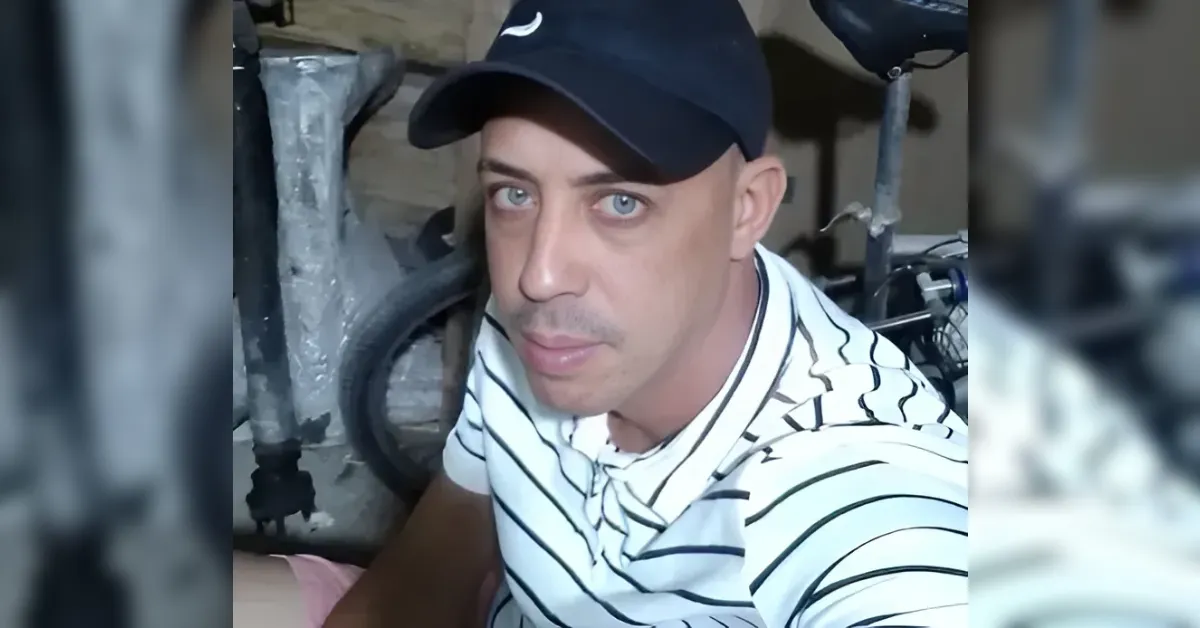 Man wearing a black cap and striped polo sits in a cluttered workshop with tires and tools in the background.