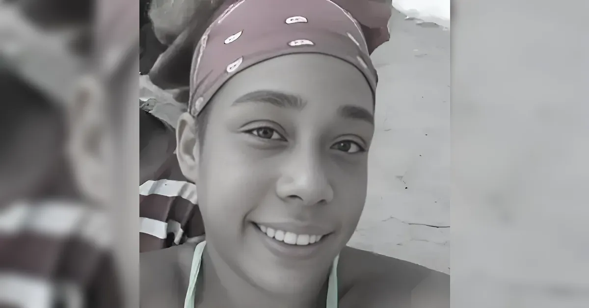 Close-up portrait of a smiling person wearing a maroon bandana with small white designs, looking at the camera in grayscale tones