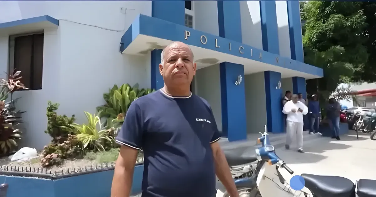 Man stands in front of a blue-and-white police station with 'POLICÍA' on the facade; a scooter is nearby.
