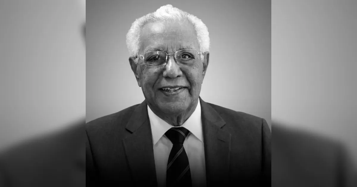 Older man with white hair and glasses wearing a dark suit and striped tie, smiling at the camera (black and white portrait).","Smiling elderly man in a suit and tie, wearing glasses, in a grayscale head-and-shoulders portrait.","Portrait of an older gentleman in a suit and tie, smiling; black-and-white photo.","Professional grayscale portrait of a senior man in a suit and glasses.