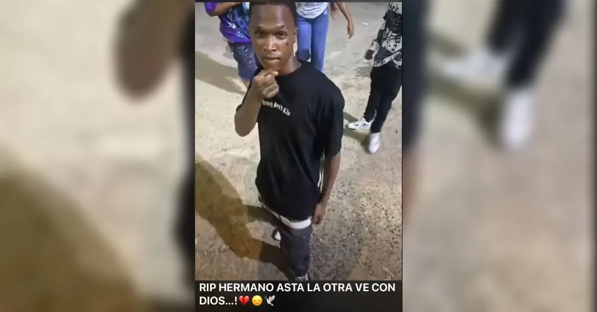 Young man in a black T-shirt stands on a rough street looking at the camera, with a small crowd in the background; caption mourning a brother going to God is overlaid.