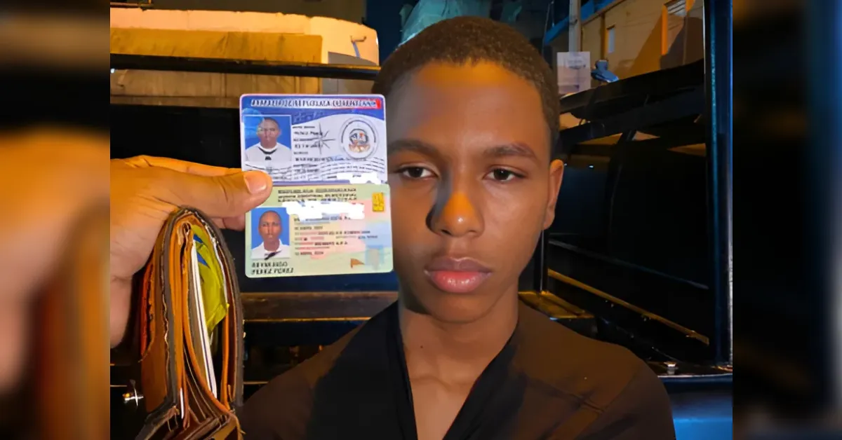 Young man facing the camera as someone holds up an identification card with his photo, at night on a street setting.