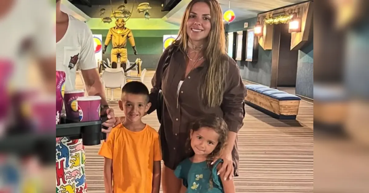 Woman with two smiling children posing at a colorful bowling alley, with lane and arcade decor in the background.