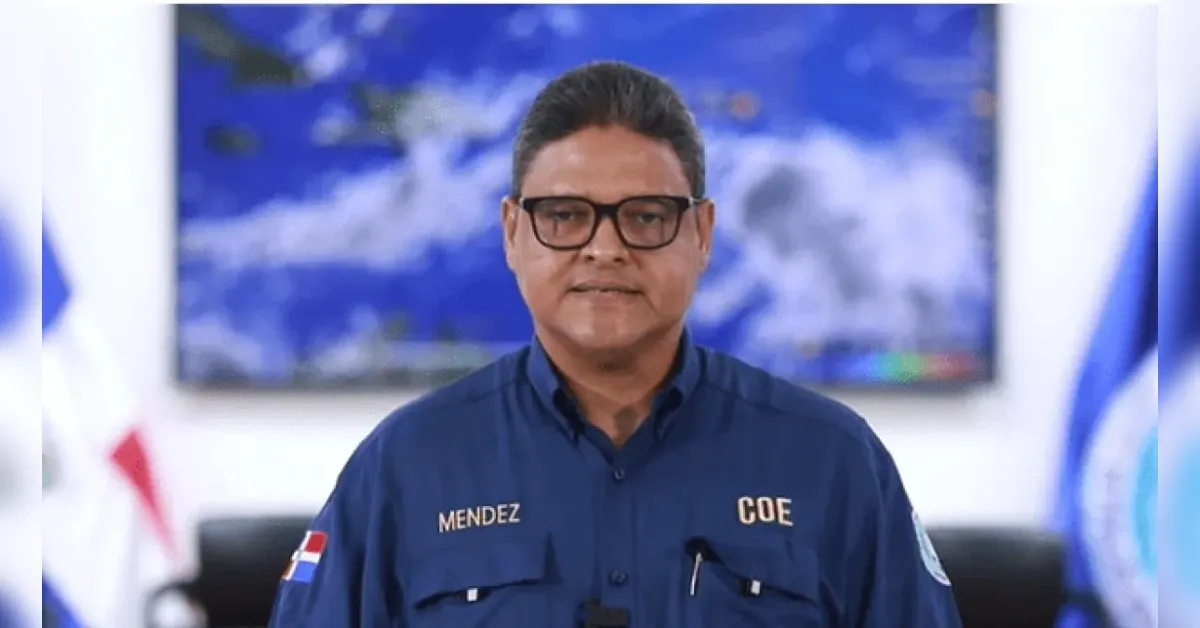 Portrait of Mendez in a blue COE uniform with a Dominican flag patch, standing in an office setting.