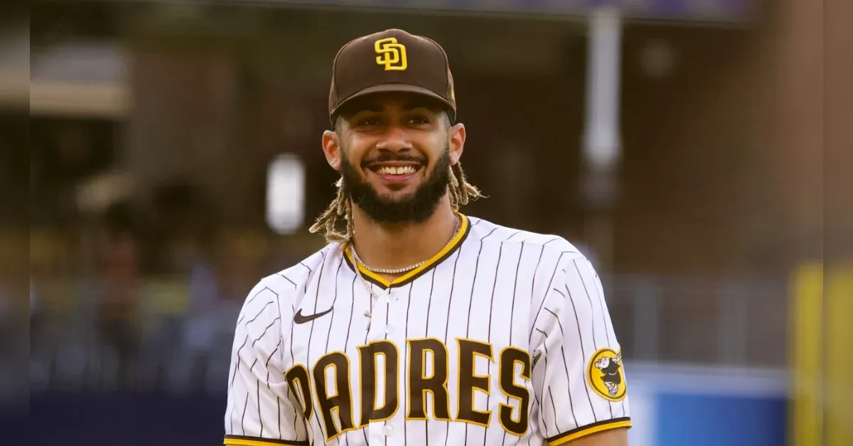 Smiling baseball player in a Padres white pinstripe jersey and brown cap, standing on the field.