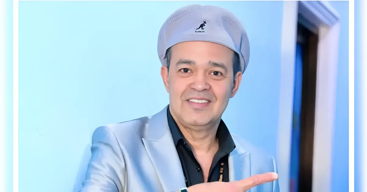 Smiling man in a pale blue blazer and light cap points to the right
