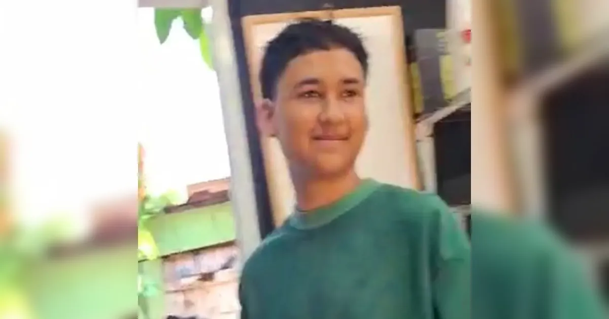 Young man with short dark hair wearing a green shirt, standing indoors near a doorway, smiling slightly.