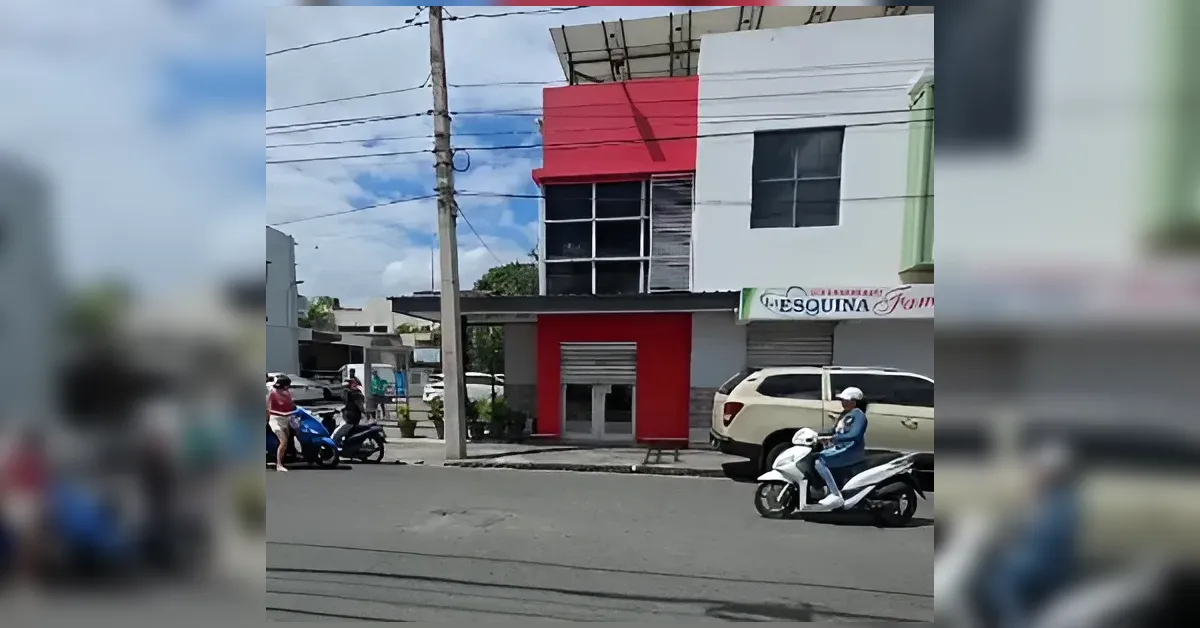 Street scene with a two-story red-and-white building and people on scooters along the curb
