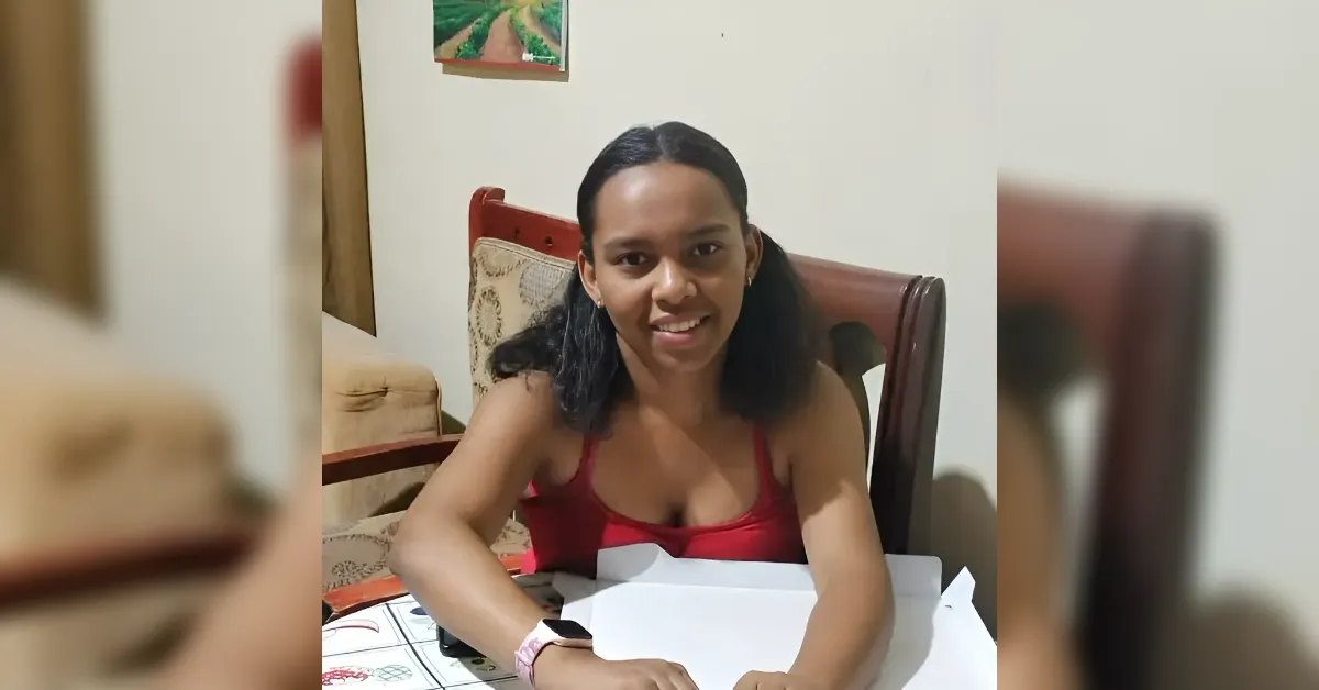 Smiling woman with shoulder-length dark hair in a red sleeveless top sits at a table with papers in front of her.