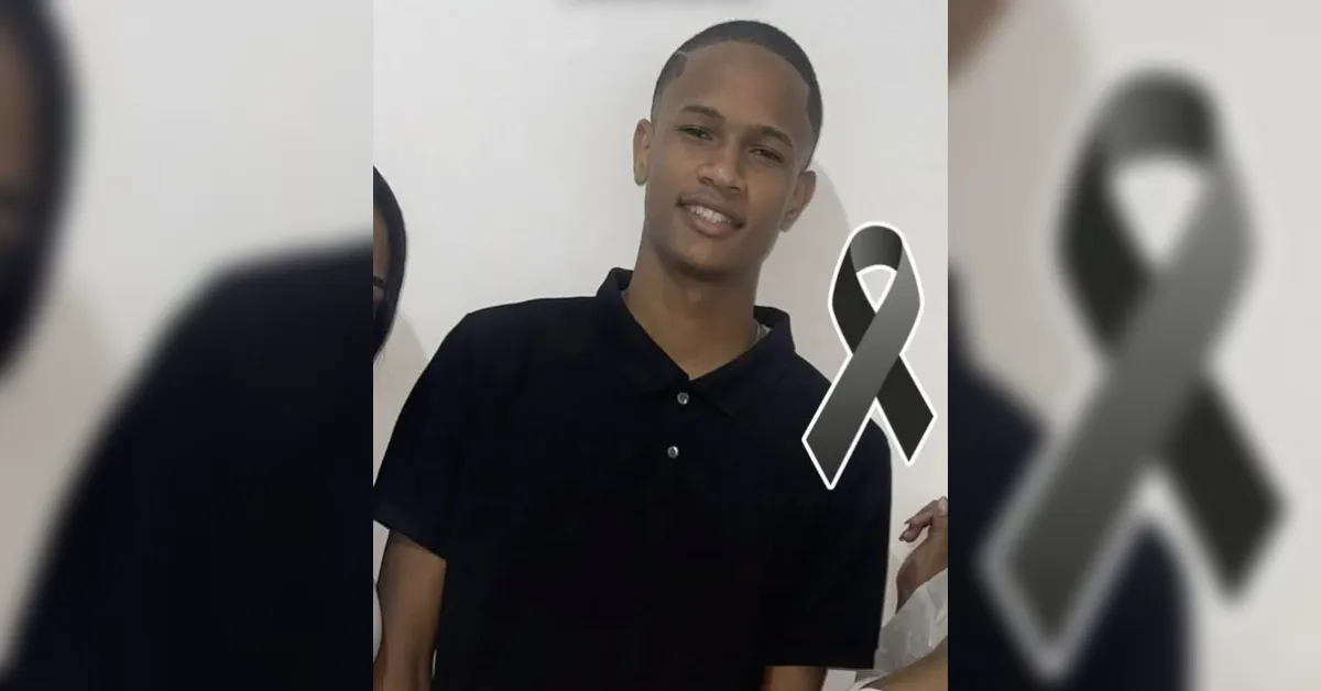 Smiling young man in a black polo shirt against a light wall, with a gray awareness ribbon overlay on his chest area.