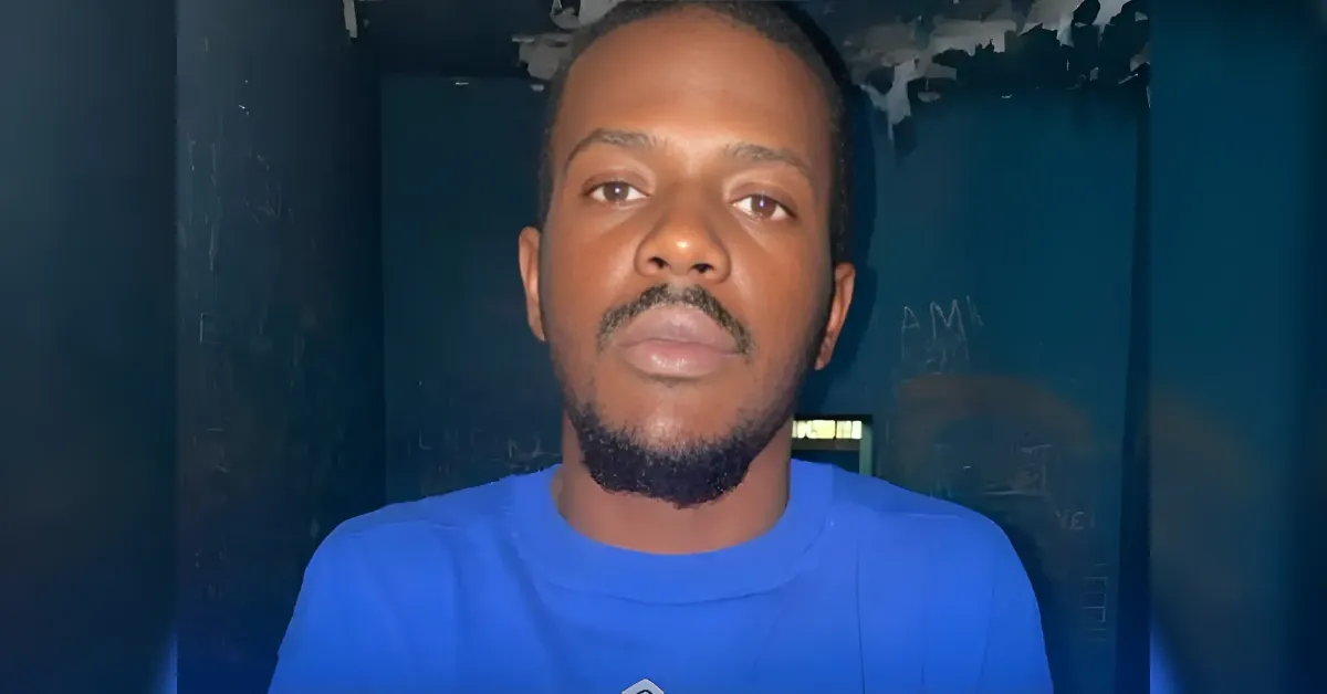 Close-up of a man with a short beard wearing a blue shirt, facing the camera in a blue-toned room.
