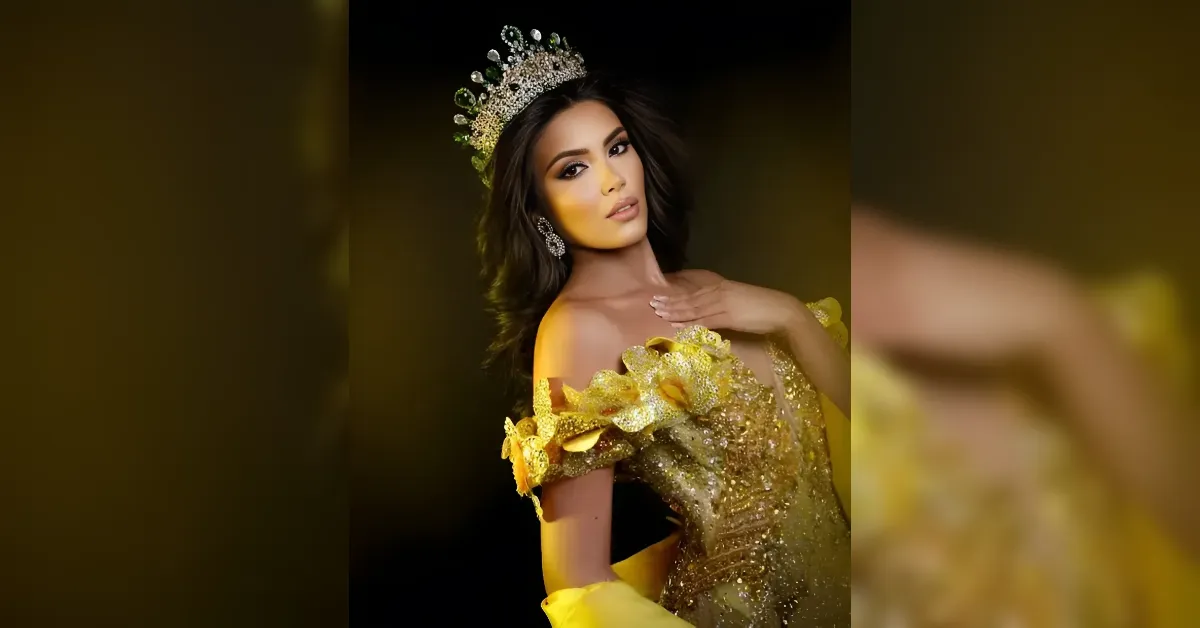 Portrait of a woman in a jeweled crown and a shimmering yellow gown, posed with her hand on her chest against a dark background.