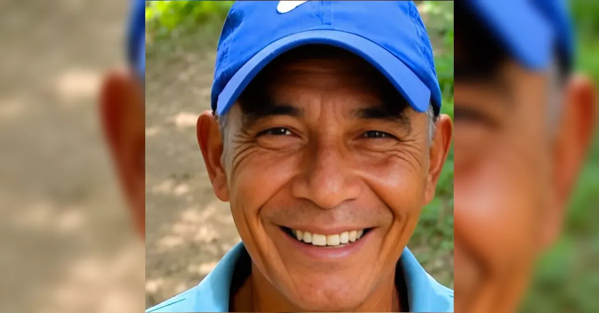 Close-up of a smiling man wearing a blue cap outdoors, showing his teeth and wrinkles around his eyes.