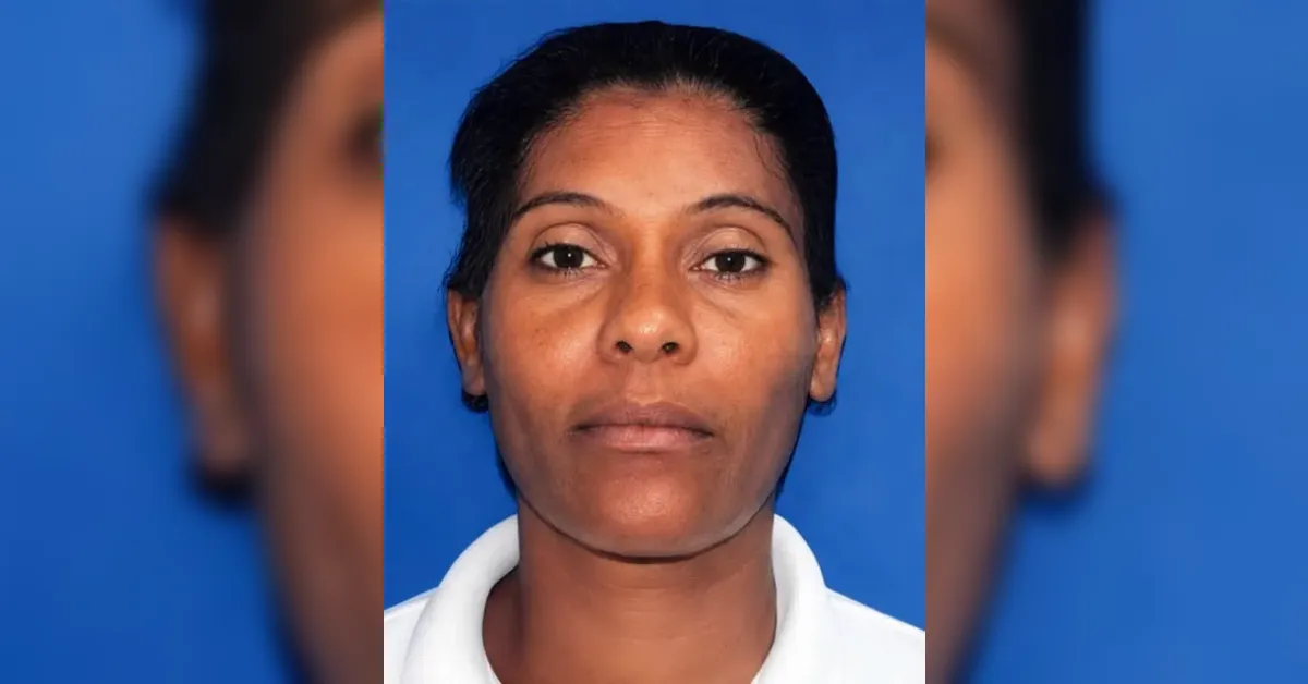 Head-and-shoulders portrait of a woman with a neutral expression against a blue backdrop, wearing a white collared shirt, looking straight ahead.