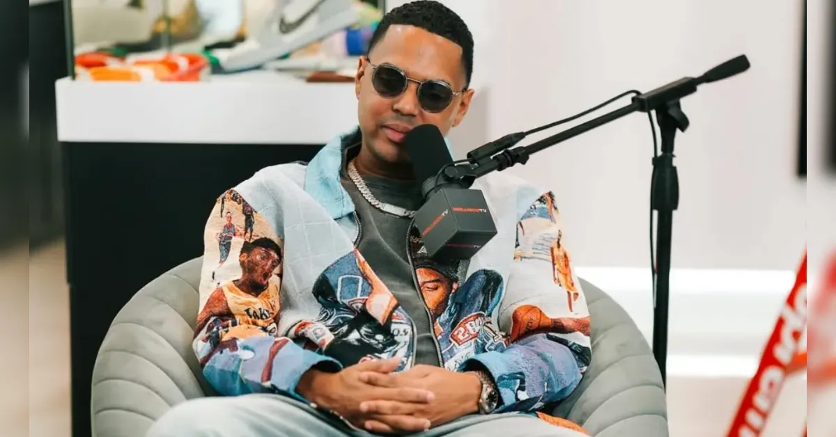 Man wearing sunglasses in a colorful jacket sits in a podcaster’s chair, speaking into a microphone.