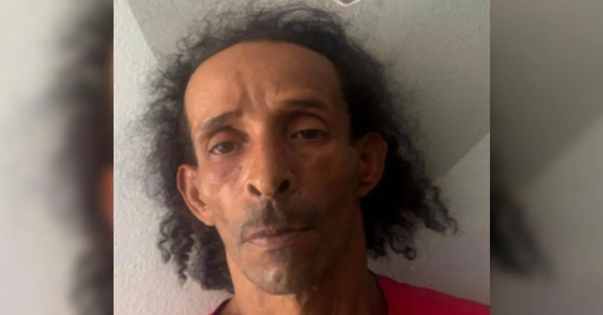 Mugshot-style photo of a man with facial injuries, wearing a red shirt, looking at the camera against a plain wall.