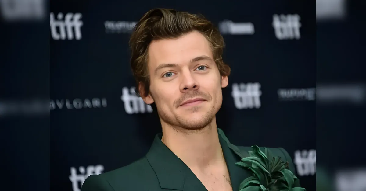 Male model on a dark red carpet wearing a dark green suit with a tropical leaf bouquet, posing at a film festival backdrop showing TIFF logos.