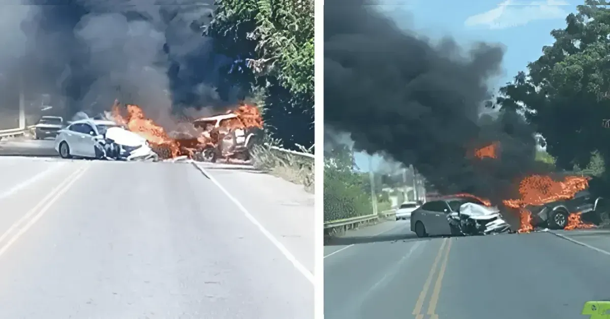 Two cars collide on a rural road, flames erupting from the wreck as thick black smoke fills the air on both sides of the road.
