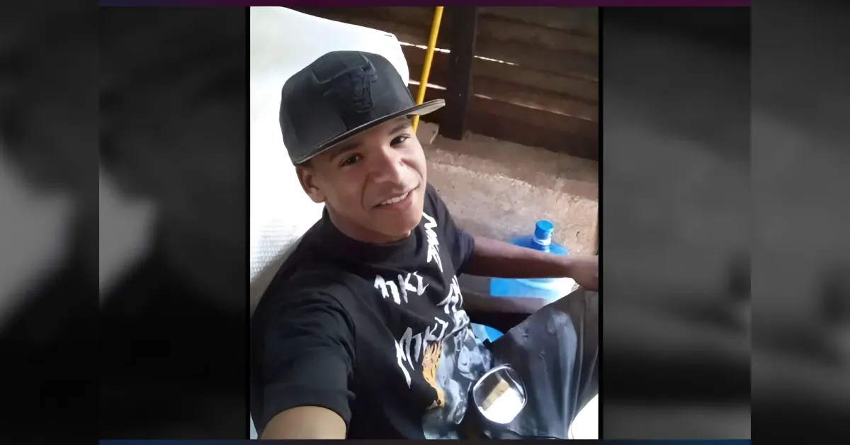 Smiling man in a black cap and T-shirt takes a selfie outdoors, with a blue water bottle nearby.