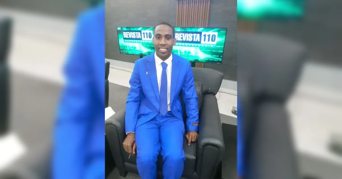 Man in a bright blue suit seated in a studio chair, with two green 'REVISTA 110' screens behind him on a news set.