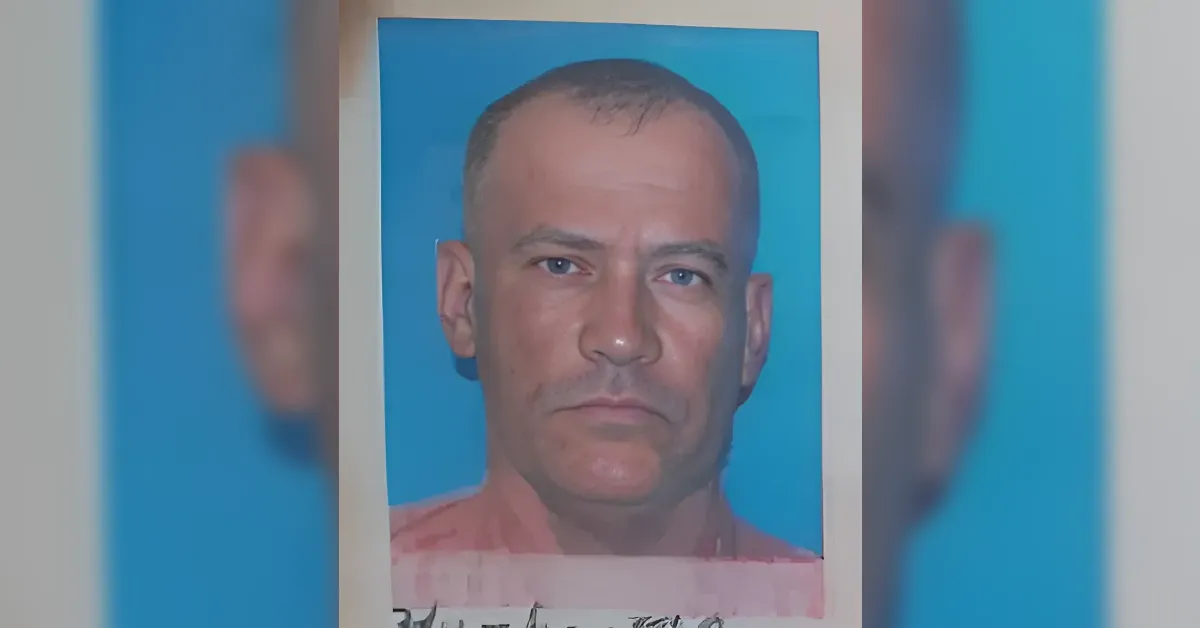 Mugshot-style photo of a man with short dark hair and a neutral expression against a blue background.
