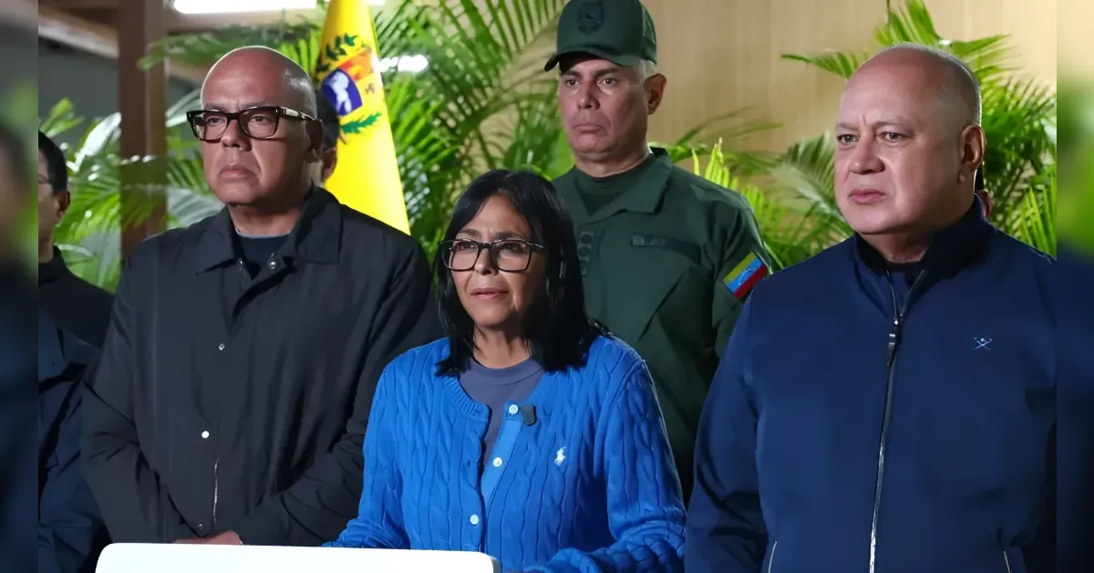 Group of three civilians and a military guard at a press conference, with a flag and plants in the background.