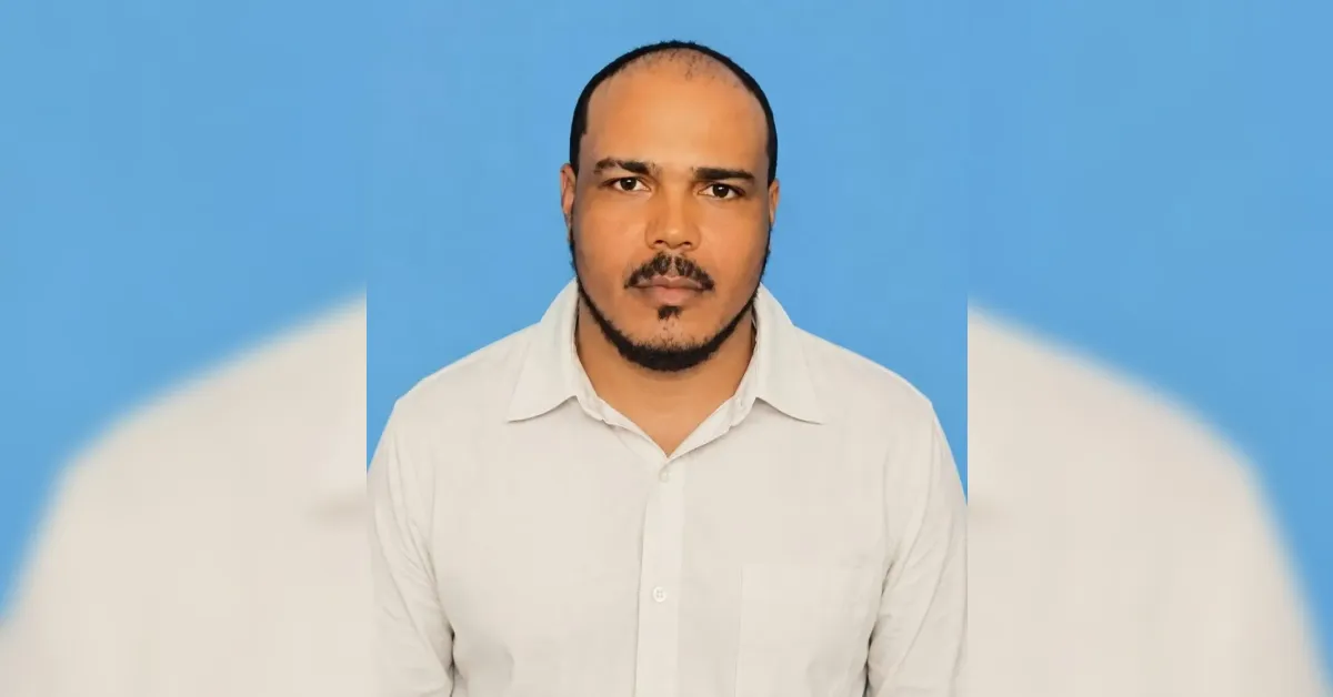 Portrait of a man with a trimmed beard wearing a white shirt against a blue background.