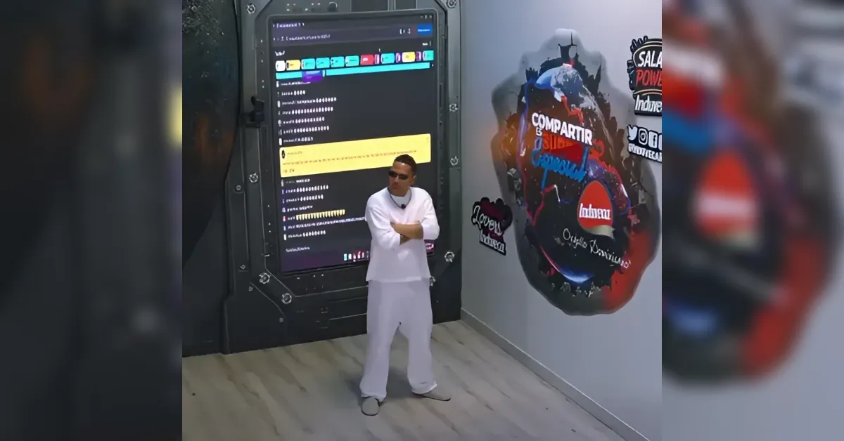 Man in white clothing stands with arms crossed in a futuristic room beside a large touchscreen showing chat-like messages.