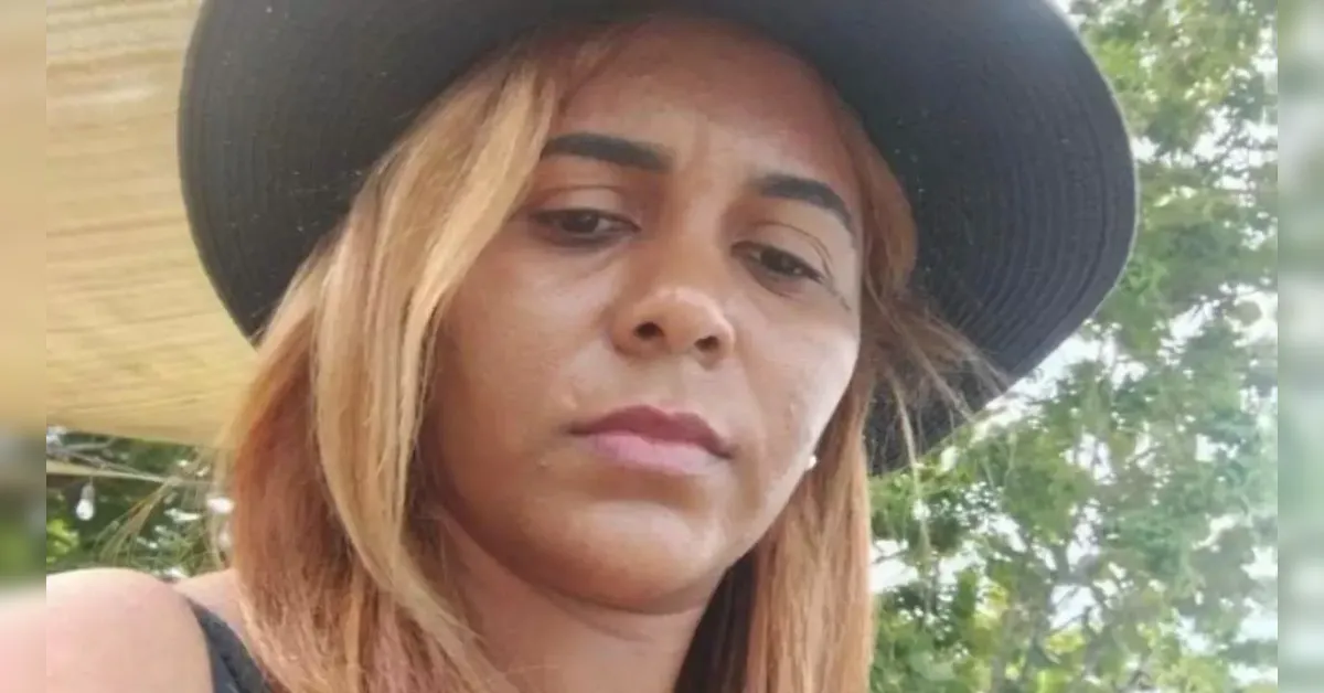 Woman with light brown shoulder-length hair wearing a wide-brimmed black hat, outdoors with trees in the background, neutral expression.