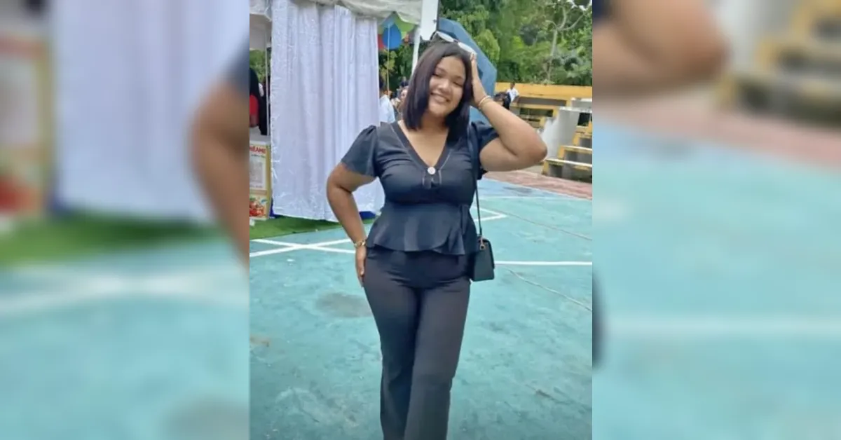 Smiling woman in a black peplum top and black pants posing with hand on hip outdoors.