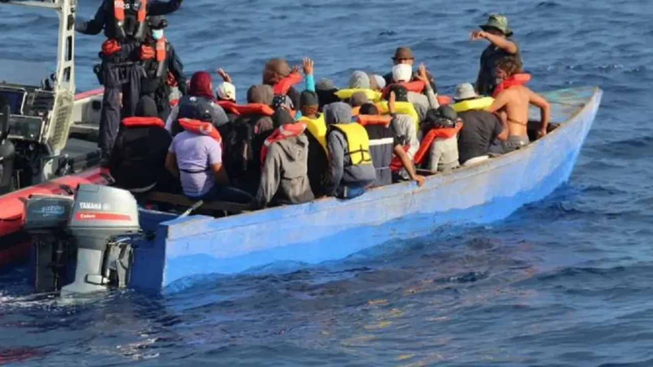 Overcrowded small boat at sea with numerous people wearing orange life jackets.