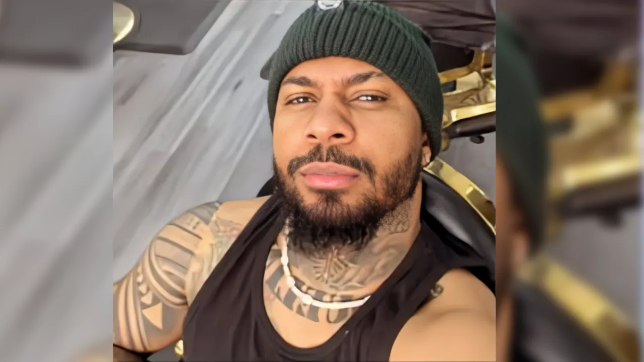 Selfie of a bearded man in a green knitted beanie and black sleeveless shirt, with visible neck and arm tattoos, looking at the camera.
