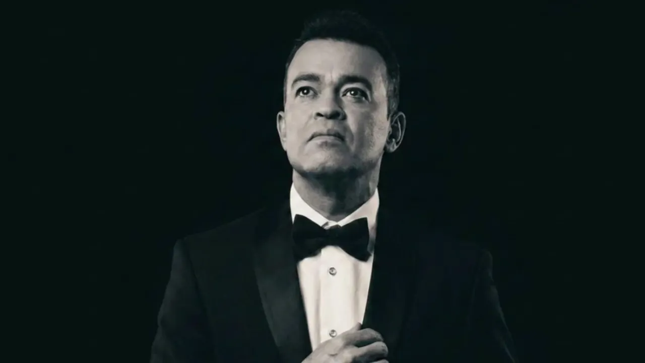 Man in a black tuxedo and bow tie looking upward against a dark background.