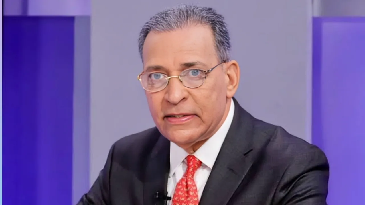Man in a dark suit and red tie speaks at a panel, wearing glasses.