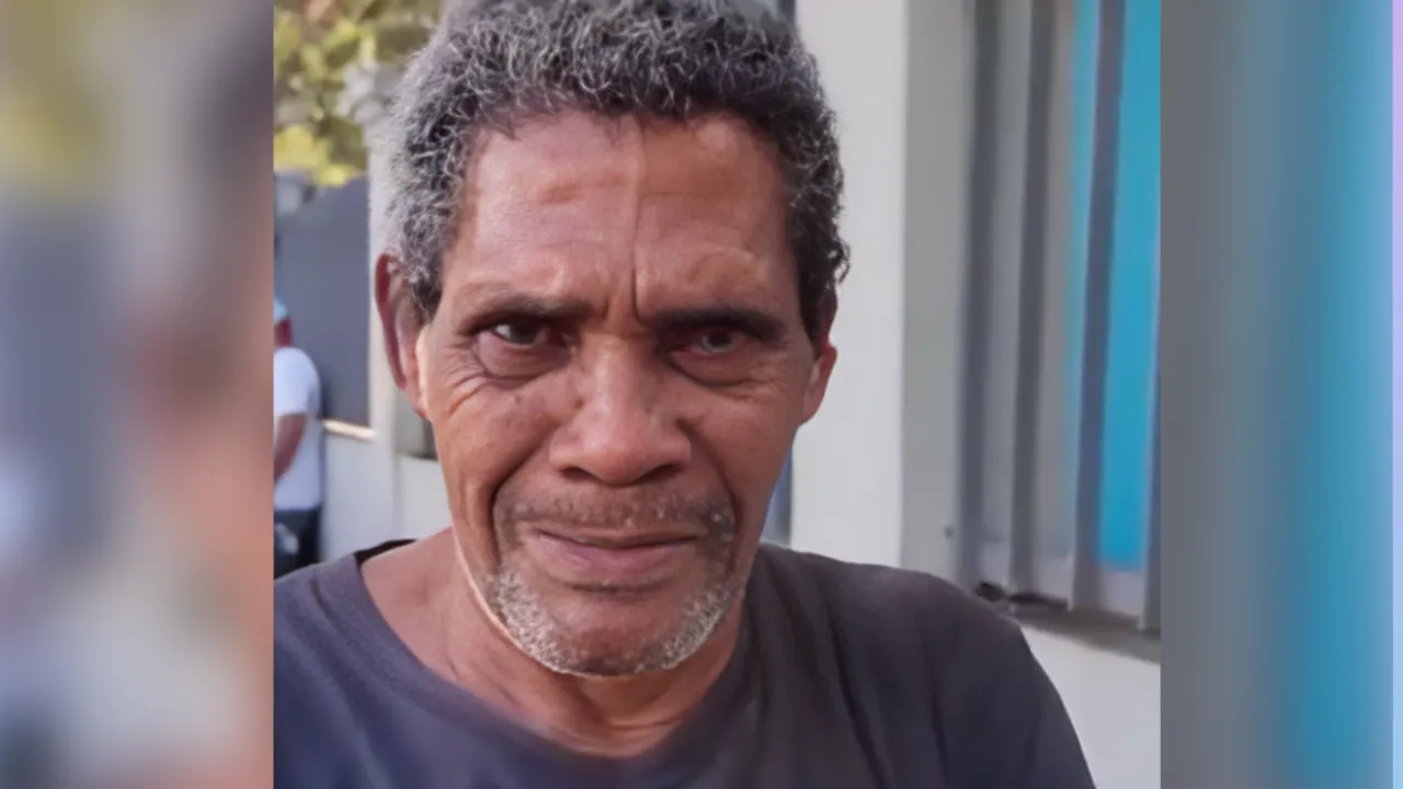 Portrait of a middle‑aged man with salt-and-pepper hair and light stubble, wearing a dark shirt outdoors beside a building.