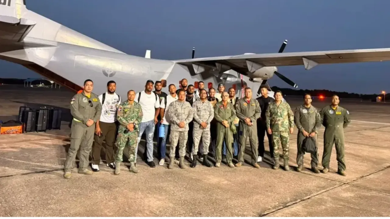 Group of military personnel in flight suits posing in front of a large cargo aircraft on an airfield at dusk.