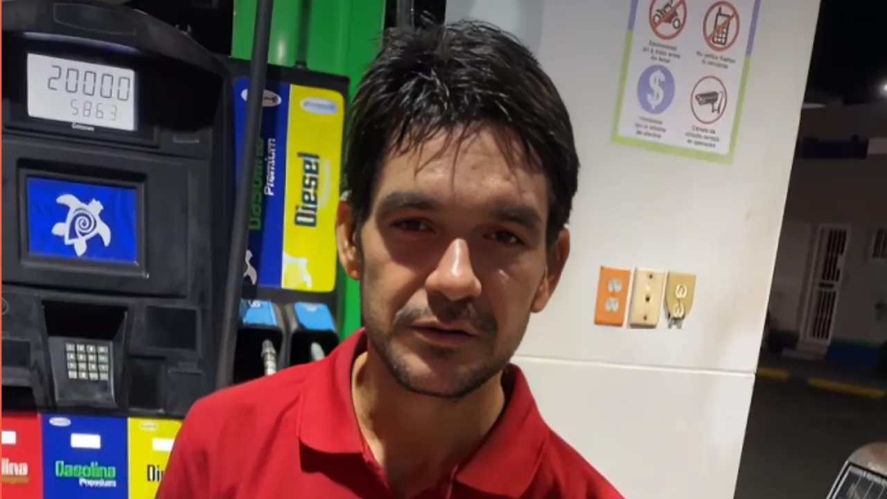 Man in a red polo standing at a gas station, colorful fuel pumps and a payment kiosk visible behind him.