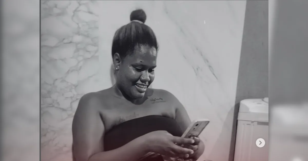 Smiling woman with a top bun wrapped in a towel, looking at her smartphone in a marble-tiled bathroom (black-and-white).