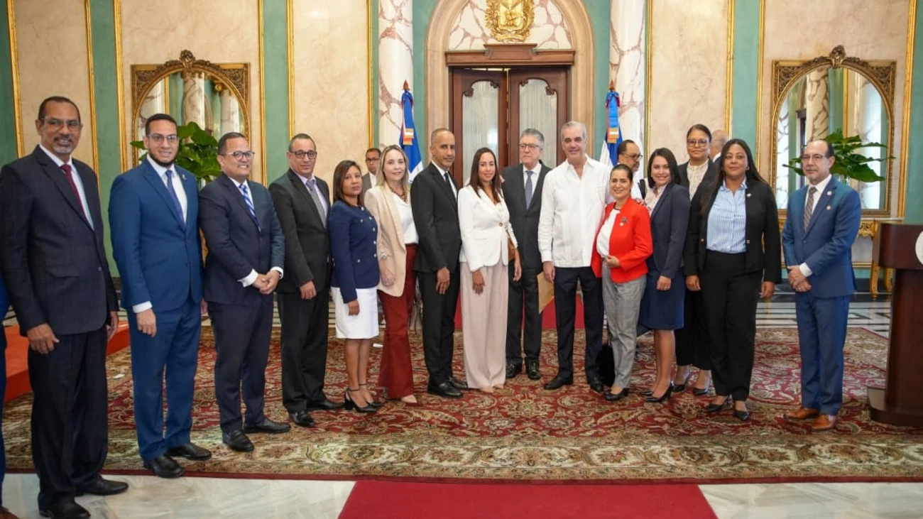 Group of formally dressed officials posing for a ceremonial group photo in an ornate government hall with marble walls and a red carpet positioned in front of a grand doorway.