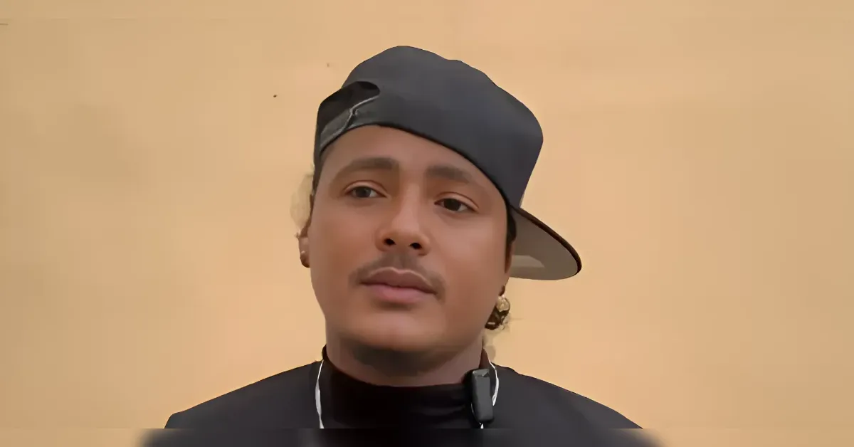 Portrait of a man wearing a backward gray cap and black shirt, neutral beige background, looking at the camera.
