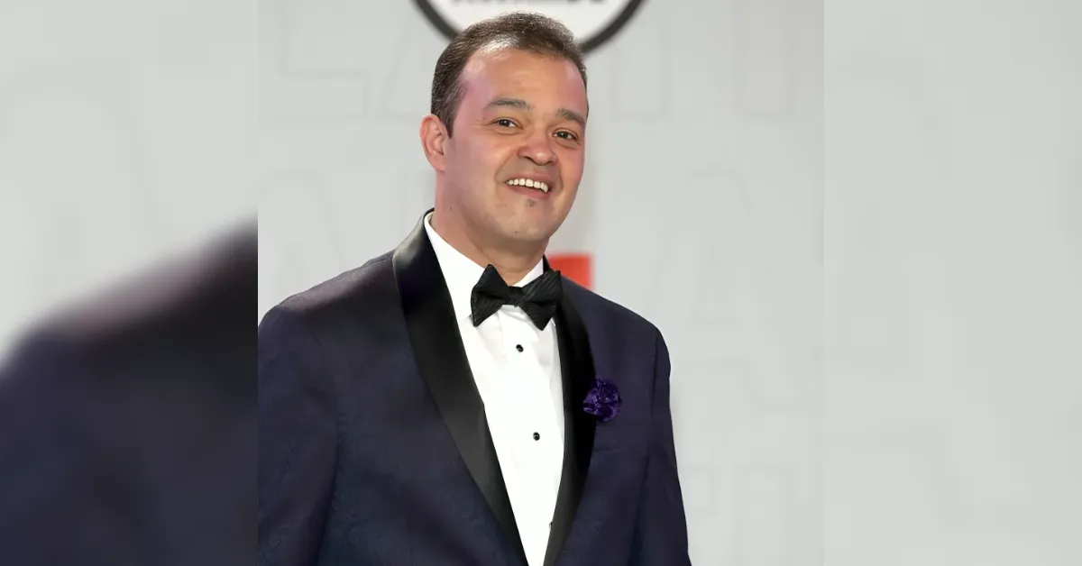 Smiling man in a dark navy tuxedo with black satin lapels and a purple boutonniere at a formal event