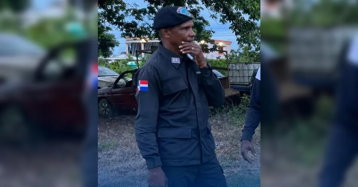 Uniformed man standing outdoors, Indonesian flag patch on his sleeve, hand near mouth as he smoke a cigarette.