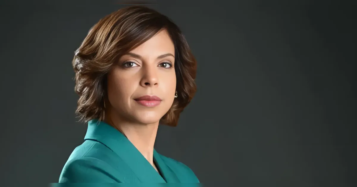 Professional headshot of a woman with short brown hair in a teal blazer against a dark background.