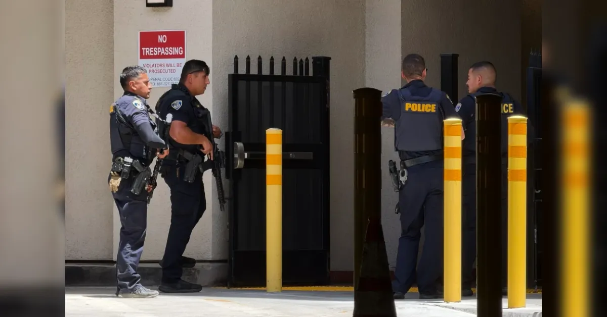 Four police officers in tactical gear guard a gated entrance beside a No Trespassing sign.
