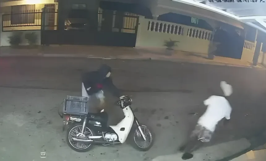 Night surveillance: a white scooter with rear rack parked on a street; two people, one in dark clothing and one in white, are nearby and moving away.