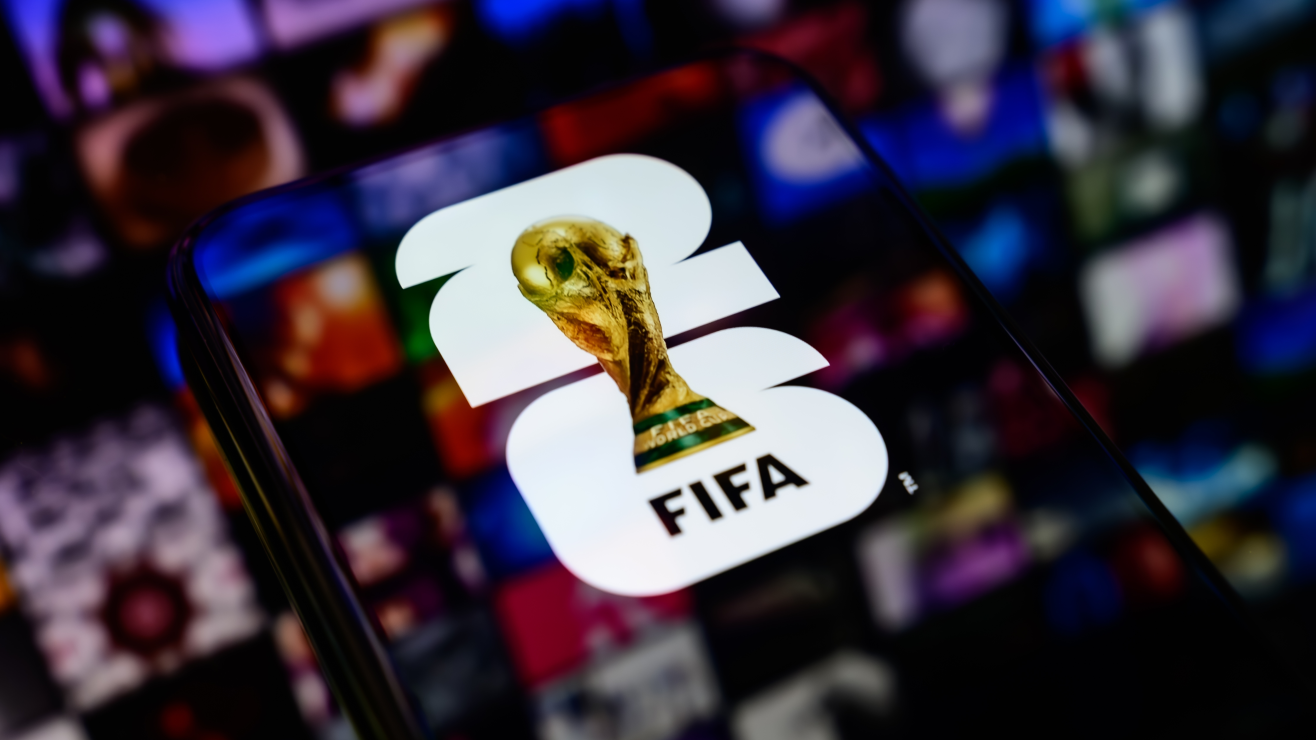 Smartphone screen displaying the FIFA app icon with a gold trophy in the foreground against a colorful blurred background.